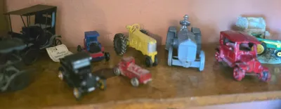 Collection of vintage die-cast toy vehicles, including tractors and early 20th-century style cars, showing some paint wear consistent...