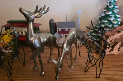Pair of vintage brass deer figurines, including a standing buck and a grazing doe, displayed alongside wire-frame deer and other holiday...