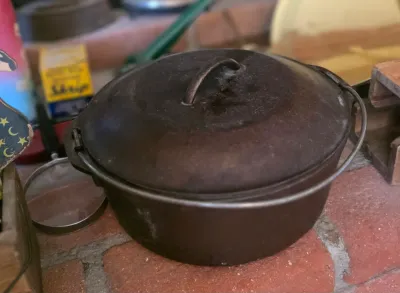 Vintage cast iron Dutch oven with matching lid and wire bail handle, showing a weathered patina.