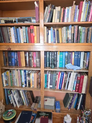 Large wooden bookshelf filled with a diverse collection of vintage and modern books, including religious texts, history, and literature,...