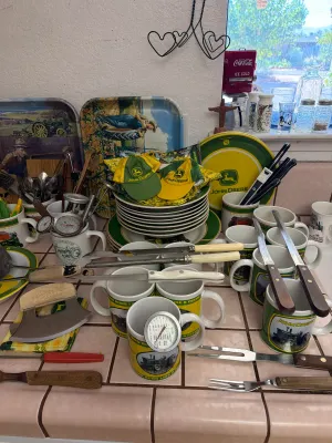 Collection of John Deere themed kitchenware and collectibles, including mugs, plates, serving trays, miniature hats, and various kitchen...