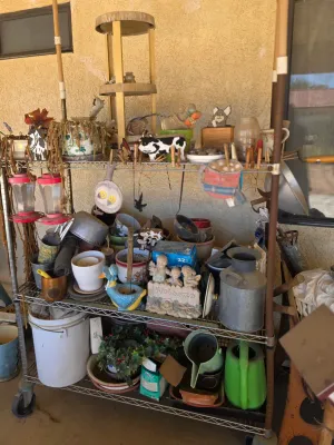 A metal wire rolling cart filled with various garden supplies, planters, watering cans, and outdoor decor items.