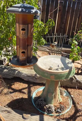 Weathered metal tube bird feeder paired with a concrete mushroom-style bird bath featuring green painted accents.