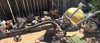 Vintage walk-behind single-bottom plow with wooden handles and iron frame, displayed alongside rustic garden decor and toy trucks.