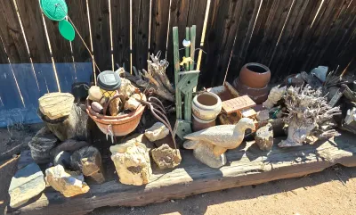 Assorted rustic garden decor, including petrified wood specimens, ceramic pots, a concrete bird statue, and a wooden birdhouse, arranged...