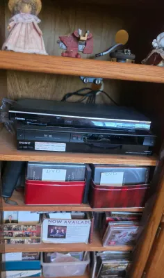 Toshiba DVD player and Sony VCR/DVD recorder combo unit stacked on a wooden shelf, with various media storage tins and cases below.