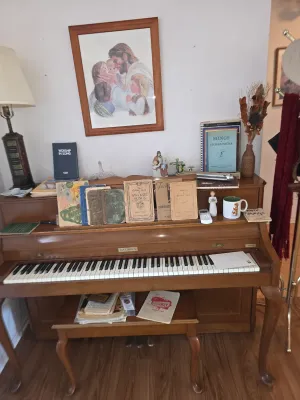 Vintage Baldwin spinet piano in a warm wood finish, complete with a matching bench and a collection of vintage sheet music and songbooks.