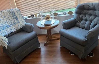 Pair of vintage blue upholstered armchairs with button-tufted backs, shown alongside a small round wooden pedestal side table.