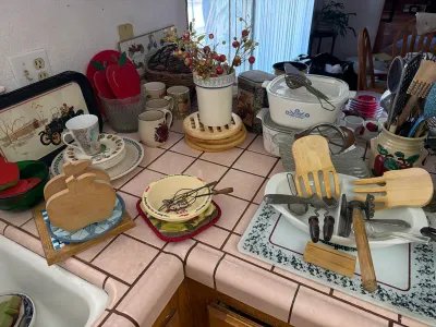Assorted vintage kitchenware, including CorningWare casserole dishes, wooden salad tongs, ceramic mugs, and apple-themed decor arranged...