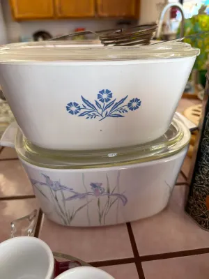Vintage Corning Ware casserole dishes with glass lids, featuring the classic Blue Cornflower pattern on top and a purple iris floral...