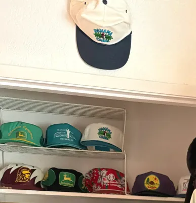 Collection of vintage trucker hats and baseball caps, including John Deere, Panama Canal, and other graphic designs, displayed on a wire...