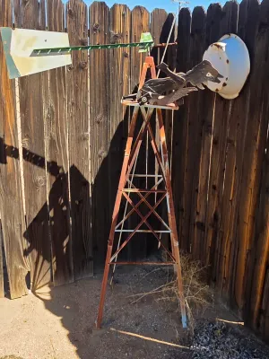 Vintage metal garden windmill with a weathered, rusty finish and a wooden bird figure mounted on top.
