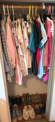 Assorted women's clothing hanging in a closet, including blouses and shirts in various patterns and colors, with several pairs of...