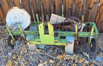 Vintage green pull-behind farm implement with small rubber wheels, a rusty metal wheel, and an enamel basin, showing significant wear and...