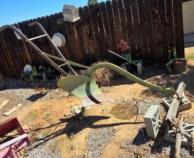 Vintage walk-behind garden plow with a green-painted metal frame and wooden handles, showing some rust and wear consistent with age.