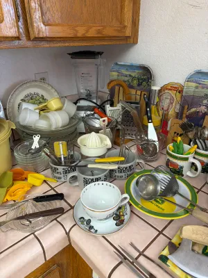 Assorted vintage kitchenware and utensils, including John Deere themed plates and mugs, soup bowls, measuring cups, and a Blendtec blender.
