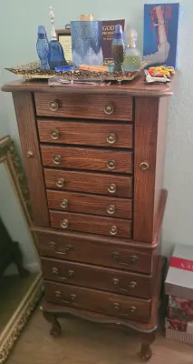 Vintage oak standing jewelry armoire featuring a flip-top lid, side doors, and multiple drawers with brass hardware, resting on cabriole...