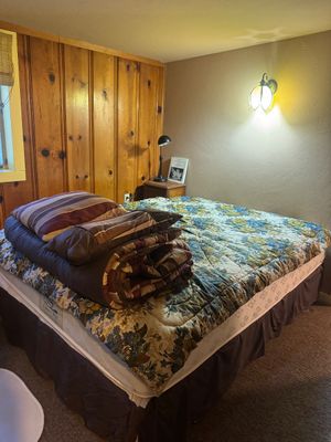 Double bed with a floral patterned quilt, striped pillows, and a brown bed skirt, set against a wood-paneled wall.