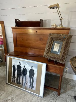 Antique wooden slant-front desk with a brass desk lamp, an ornate framed portrait, and a large framed U2 "No Line on the...