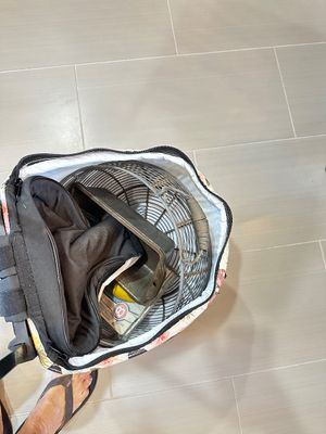 Assorted vintage items packed inside a floral rolling tote bag, including a metal wire basket, a cast iron pan, and a black fabric bag.