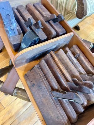 Collection of antique wooden hand planes stored in a divided wooden tote, showing wear consistent with age and use.