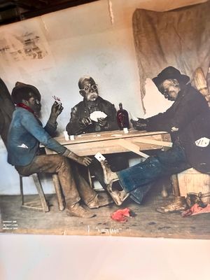 Vintage hand-colored print titled "A Skin Game," depicting three men playing cards around a wooden table, copyrighted 1898 by...