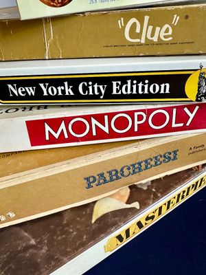 Stack of vintage board games showing some wear, including Clue, Monopoly New York City Edition, Parcheesi, and Masterpiece.