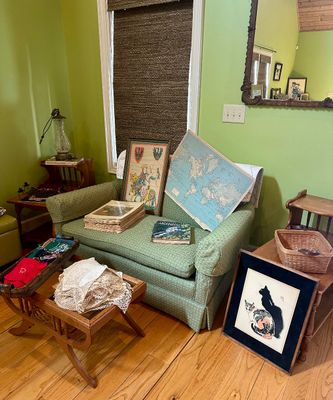 Upholstered green armchair displaying vintage items, including a framed medieval-style print, a world map, and books, surrounded by...