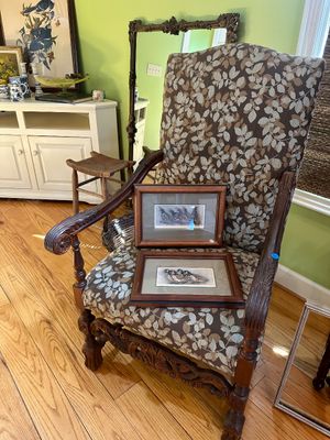 Ornate carved wood armchair with leaf-patterned upholstery, shown with two framed bird prints resting on the seat.