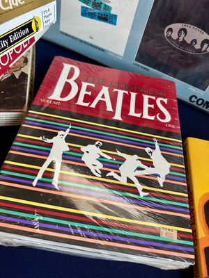 "The Compleat Beatles Volume One" sheet music book, preserved in plastic wrap, displayed alongside vintage board games and...