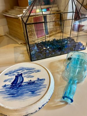Assorted decorative items including a Delft-style blue and white ceramic trivet, a violin-shaped blue glass bottle, and a glass terrarium...