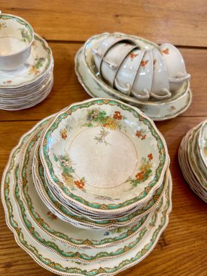 Vintage porcelain dinnerware set featuring a scalloped gold-trimmed edge, green borders, and delicate floral motifs, showing some...
