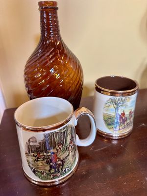 Vintage amber glass decanter with a spiral pattern, paired with two ceramic mugs featuring English fox hunting scenes and copper-toned...