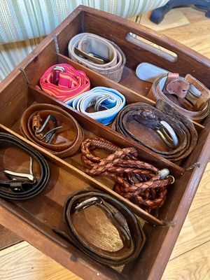 Assortment of vintage leather and fabric belts organized inside a divided wooden storage crate.