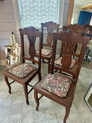 Set of four antique oak dining chairs featuring carved splats, cabriole front legs, and patterned tapestry seat cushions.