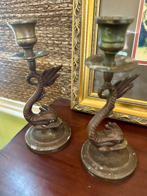 Pair of vintage brass candlesticks featuring a stylized dolphin or sea serpent design, showing some age-related patina and wear.