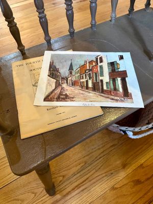 Maurice Utrillo art print titled "Eglise de Stains" resting on a 1973 Kershaw County Historical Society booklet, displayed on a...