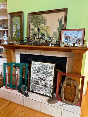 Assorted framed artwork, empty picture frames, and a black wrought iron candelabra displayed on and around a wooden fireplace mantel.