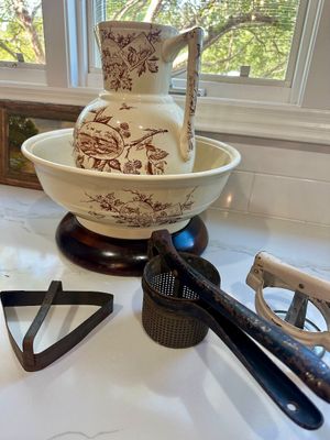 Vintage ceramic wash basin and pitcher set with brown transferware floral and bird motifs, displayed alongside antique kitchen tools...