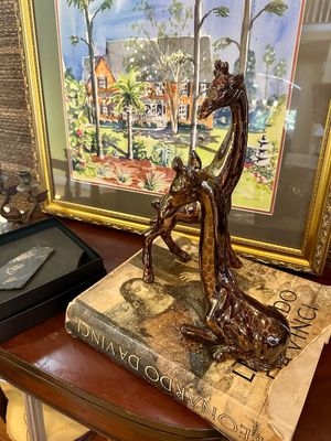Pair of glazed ceramic giraffe figurines with a metallic brown finish, displayed on a vintage Leonardo da Vinci art book.