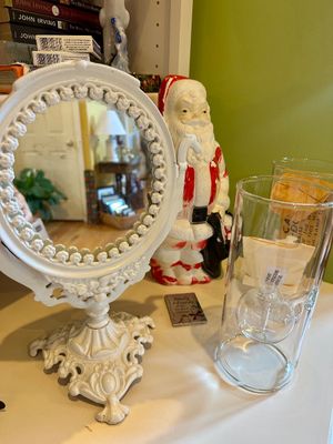 Vintage white cast iron vanity mirror with ornate scrollwork base, displayed alongside a vintage Santa Claus figurine and glass oil lamps.