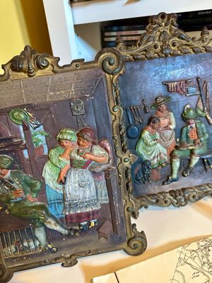 Pair of vintage cast metal relief plaques depicting traditional European tavern or cottage scenes, housed in ornate gilded frames.