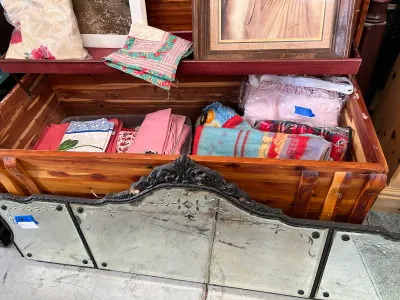Sale Photo Thumbnail #27: Vintage cedar chest filled with various linens and blankets, shown behind an ornate, etched glass tri-fold vanity mirror.