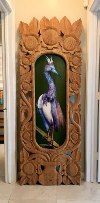 Large, intricately carved wooden floor mirror frame featuring sunflower and floral motifs, housing a vertical painting of a tricolored...