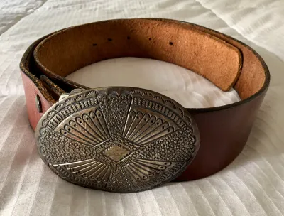 Vintage brown leather belt featuring a large, ornate silver-tone metal buckle with detailed geometric and textured engravings.