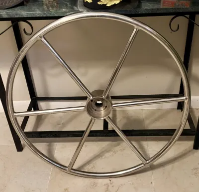 Large stainless steel destroyer-style boat steering wheel with six spokes, showing minor surface wear.
