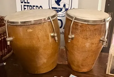 Pair of vintage wooden conga drums with natural skins and metal tuning hardware, showing some wear from use.