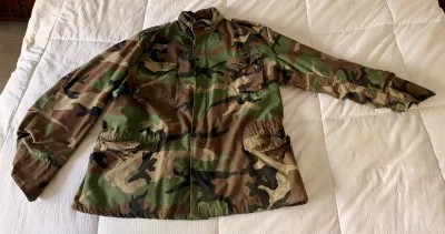 Vintage US military M-65 field jacket in woodland camouflage pattern, featuring four front pockets and a stand-up collar.