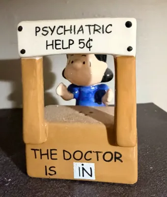 Vintage Peanuts ceramic figurine featuring Lucy van Pelt at her "Psychiatric Help 5¢" booth, with "The Doctor Is In"...