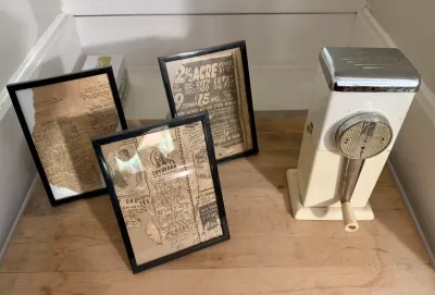 Vintage Rival Ice-O-Mat hand-crank ice crusher alongside three framed vintage newspaper advertisements.